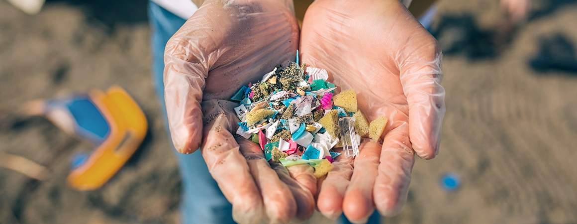 Detail of two hands holding colorful microplastics on the beach