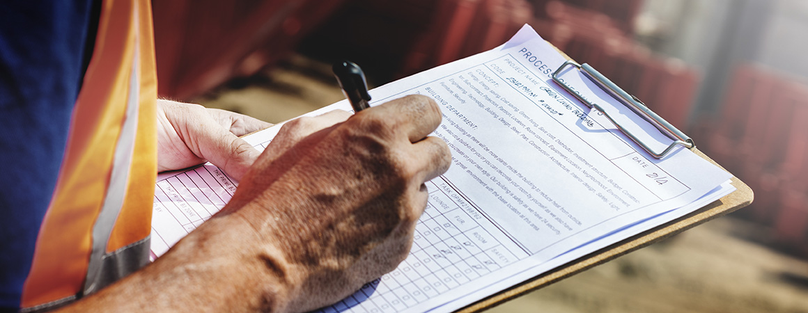 A closeup of a construction worker writing on a form while holding a clipboard. 